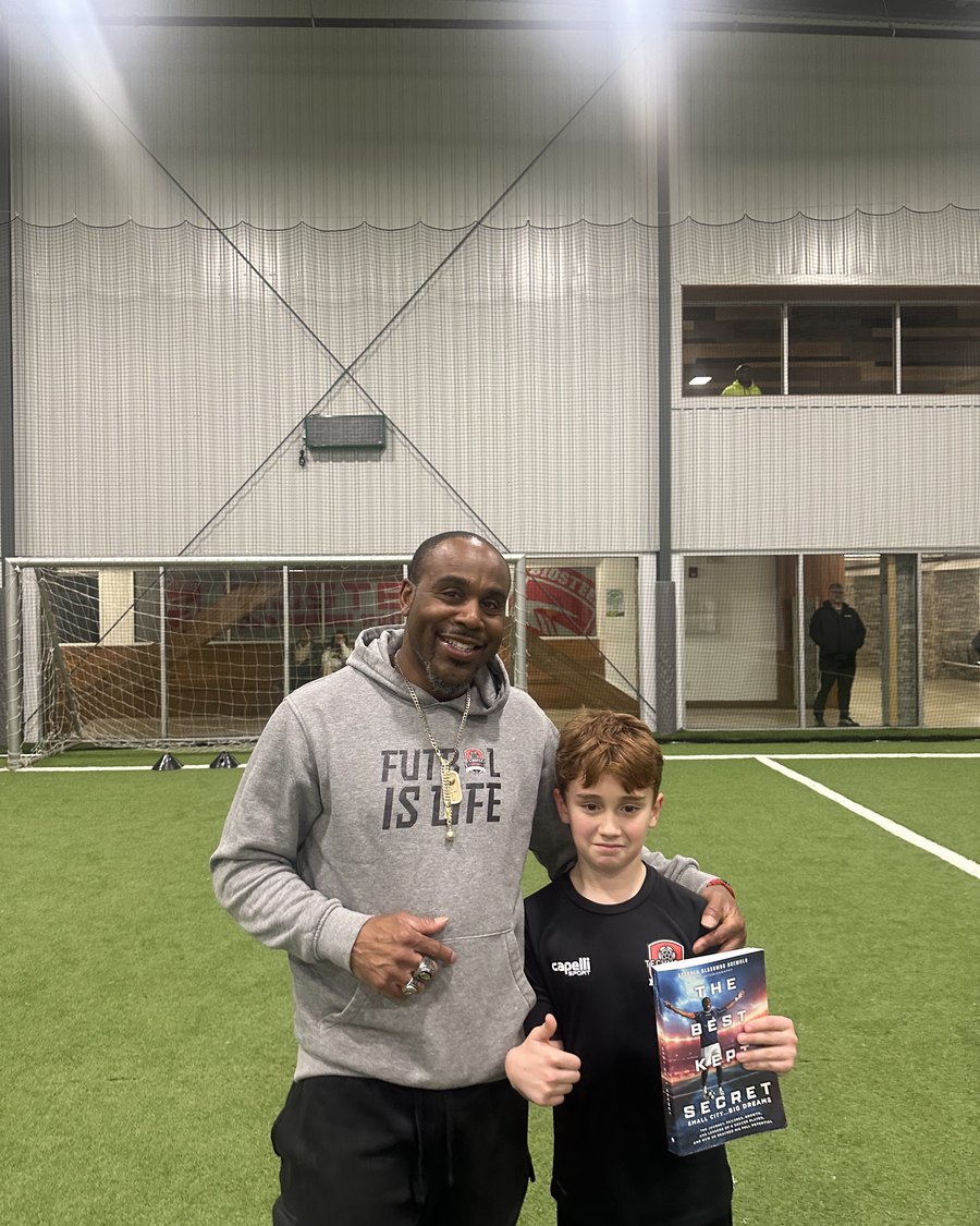 A player gives a thumbs up holding The Best Kept Secret alongside Stephen Ademolu at training